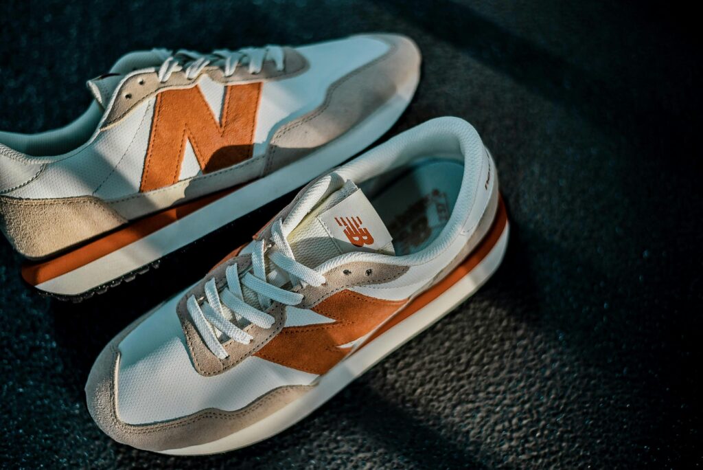 Close-up shot of New Balance sneakers with orange and white design on a textured dark background.