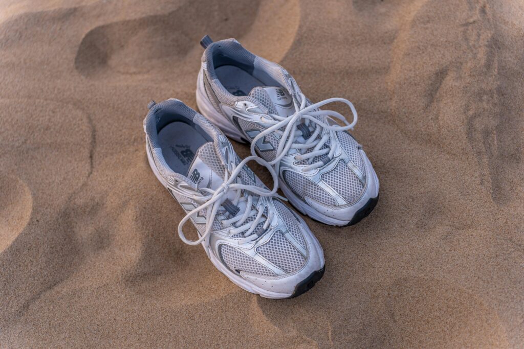 Pair of New Balance sneakers placed on sand, perfect for beach fashion concepts.
