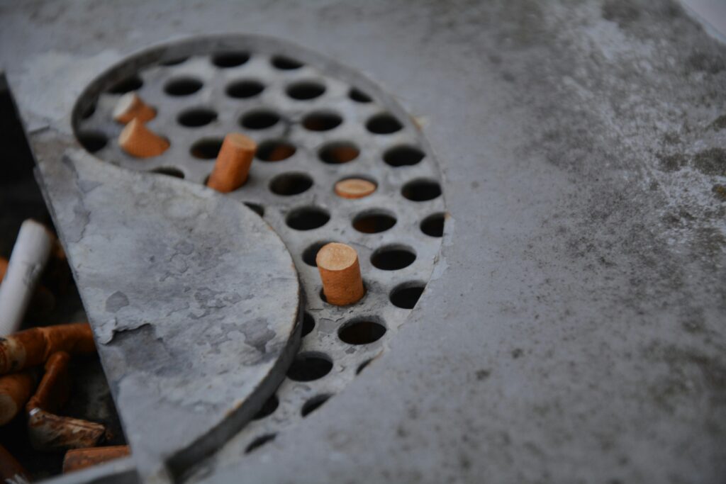 Detailed view of cigarette butts in a metal ashtray with perforated design, depicting usage and waste.