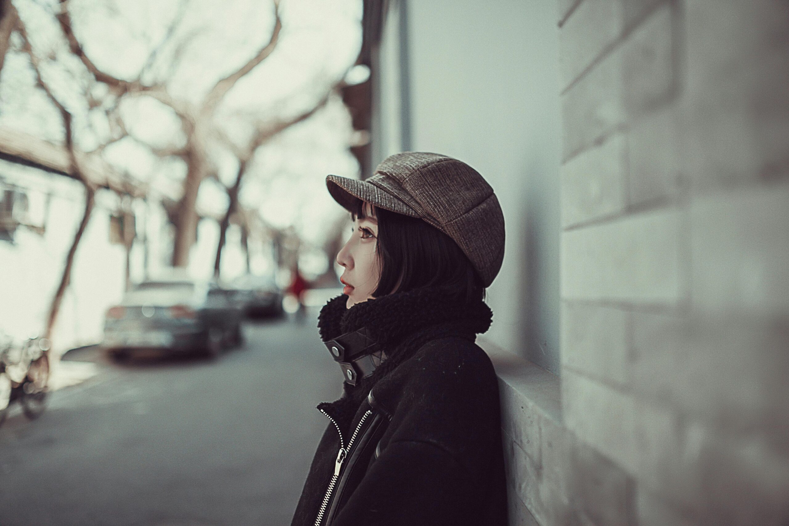 Side profile of a young woman in winter clothing, standing on a serene urban street.